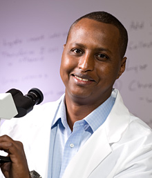 photo of Ahmed Osman, M.S. class of 2010 alumnus in front of a microscope and smiling to the camera